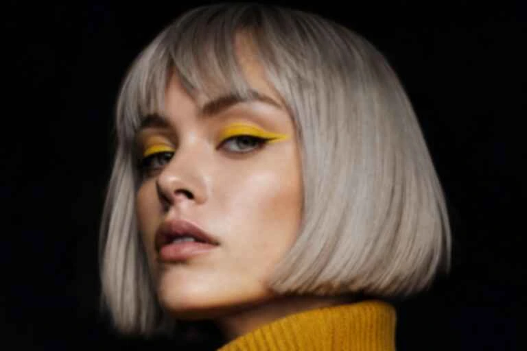 Low-resolution version of a portrait: a woman with a silver bob and yellow eyeliner